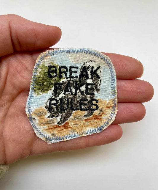 a hand holding a small patch with a skunk on it