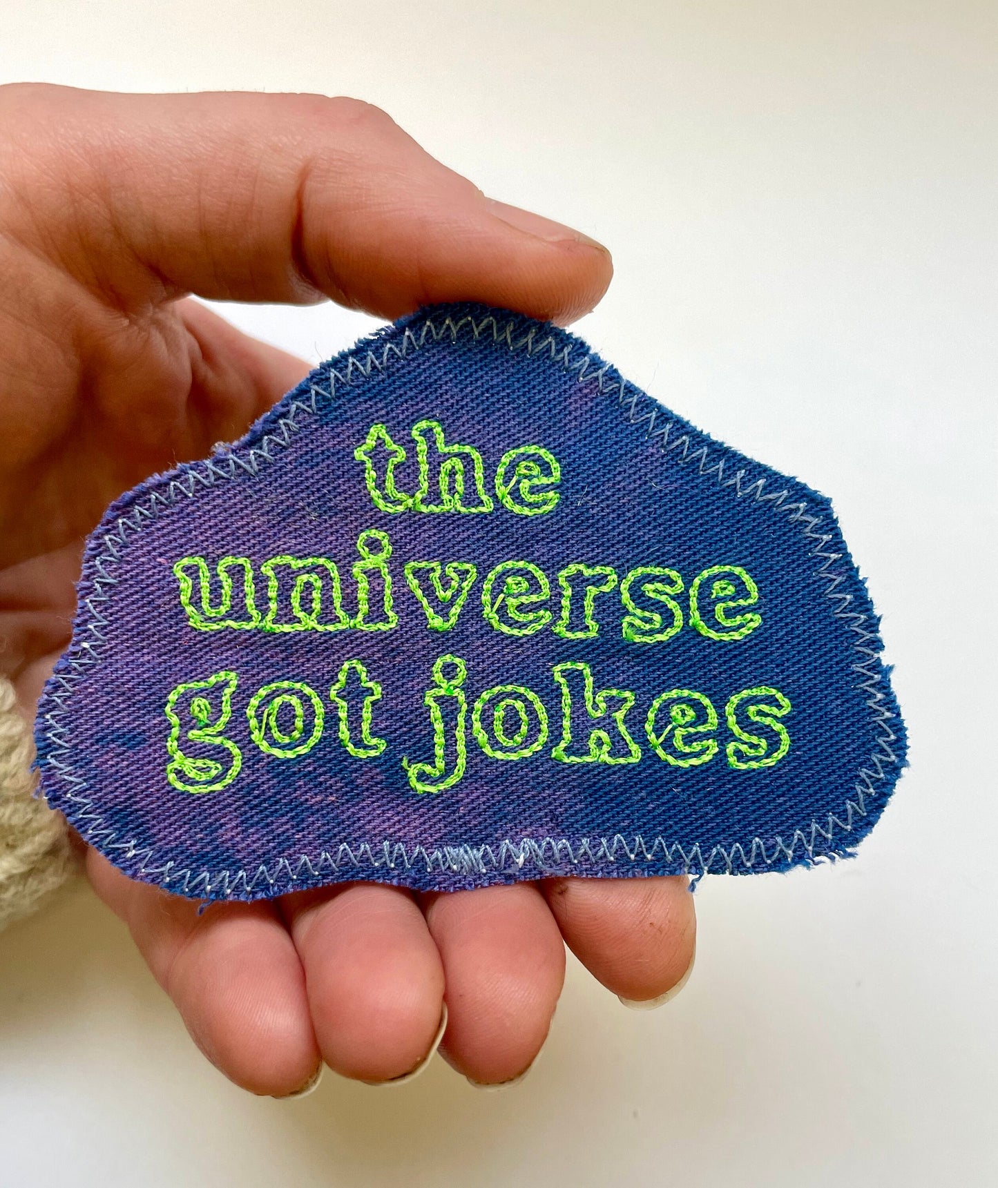 a hand holding a patch that says the universe got jokes