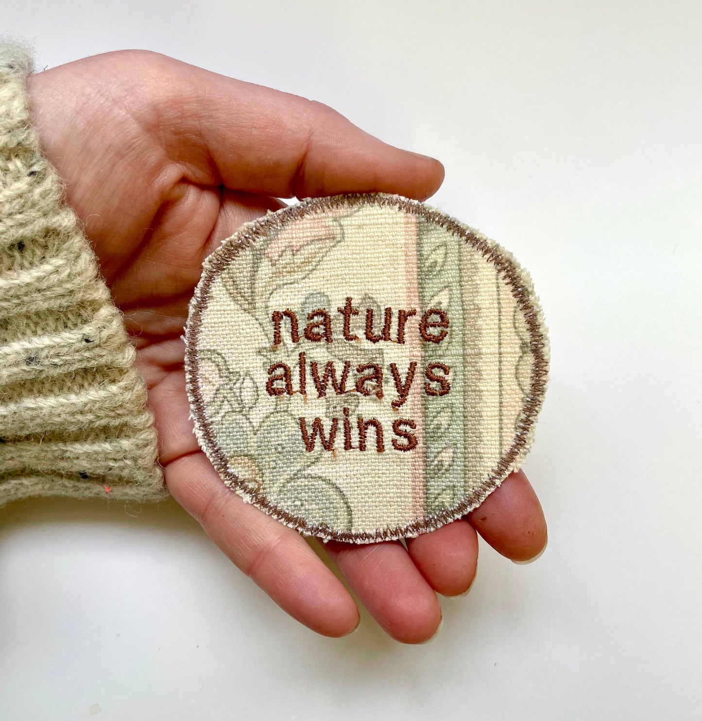 a hand holding a badge that says nature always wins