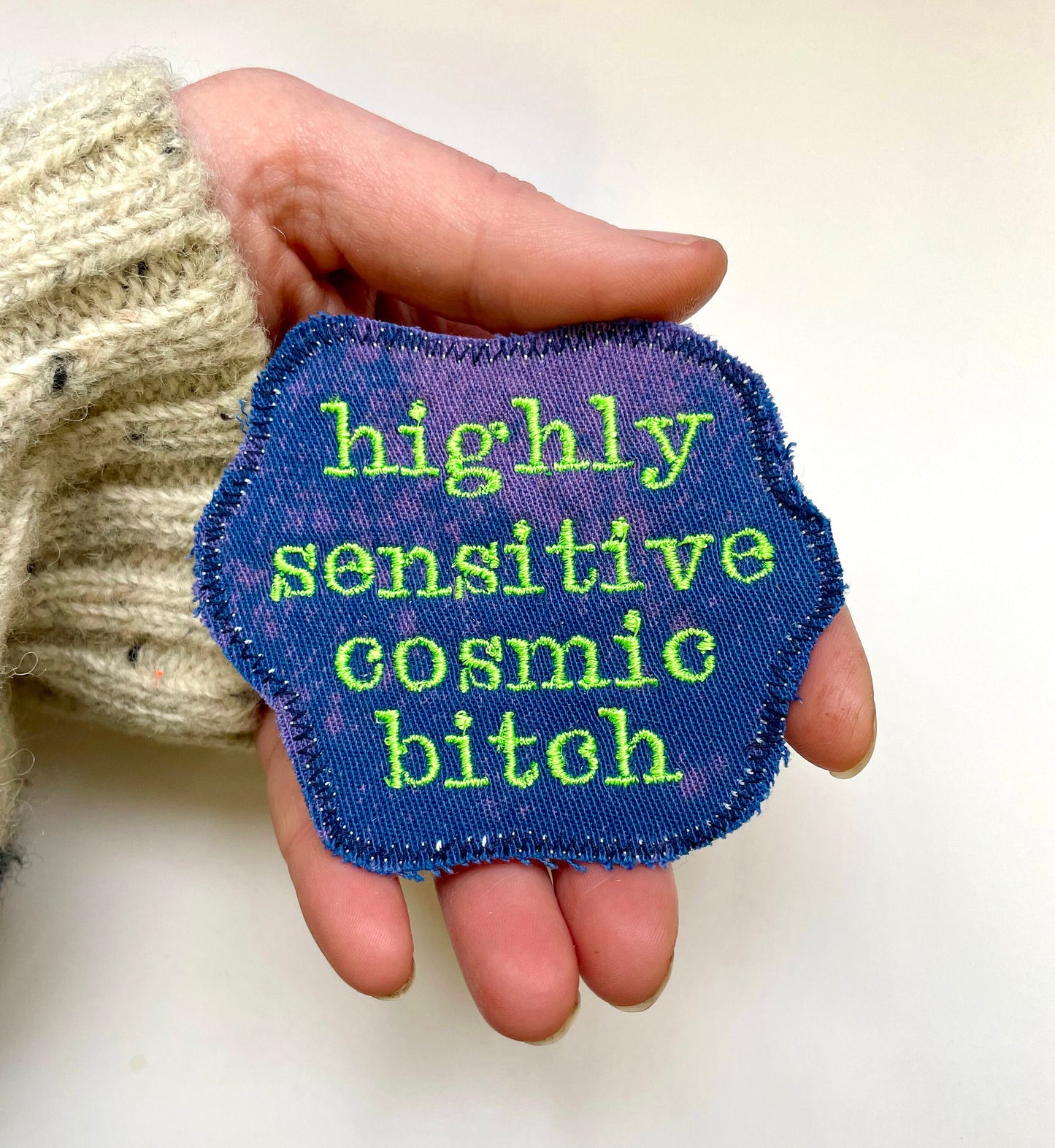 a hand holding a patch that says highly seductive cosmic bitch