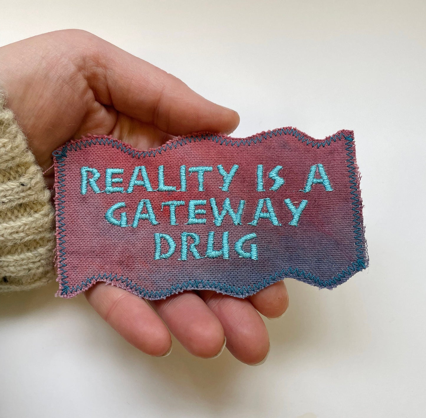 a hand holding a piece of cloth that says reality is a gateway drug