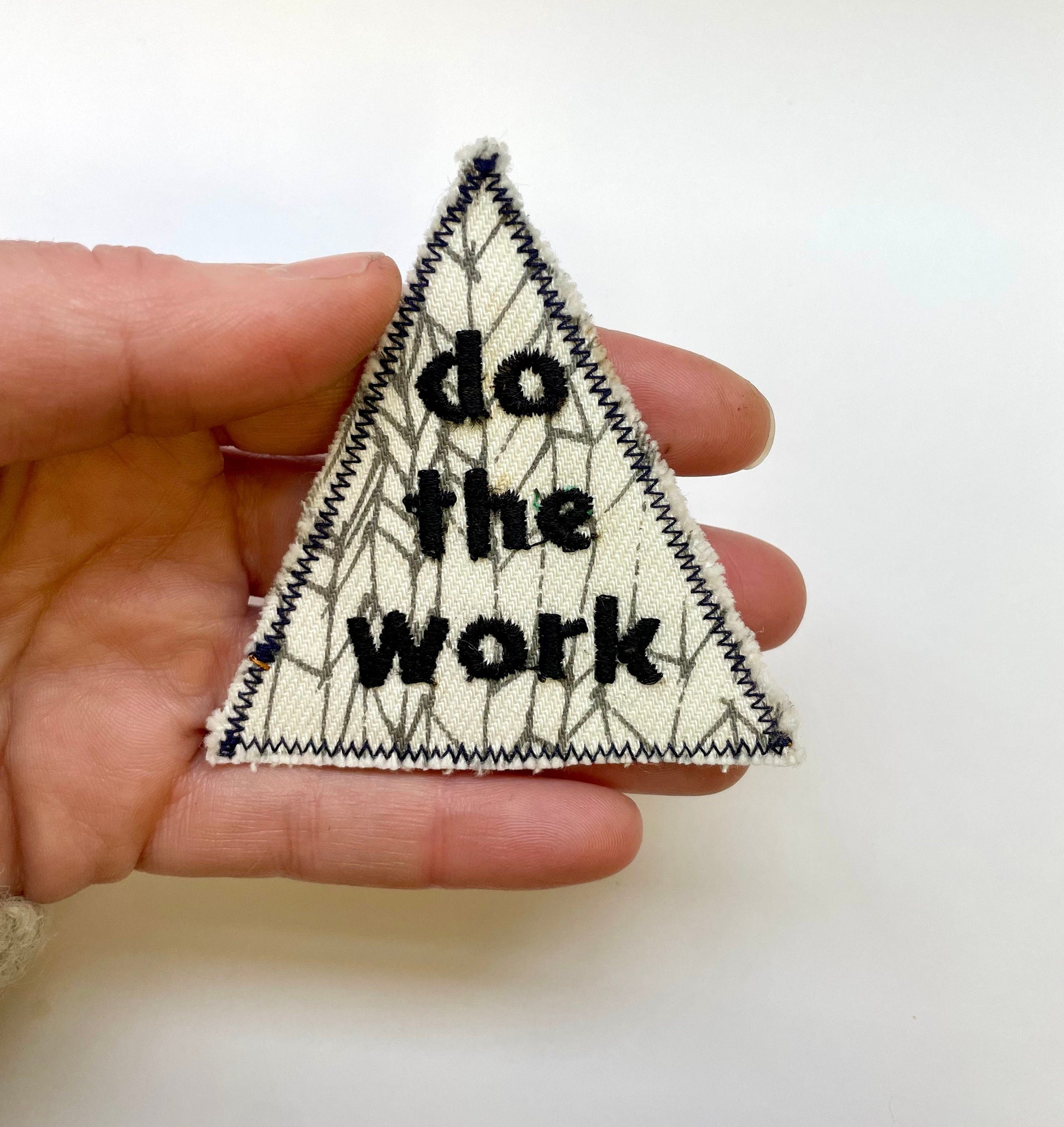 a hand holding a triangle shaped pin with the words do the work on it