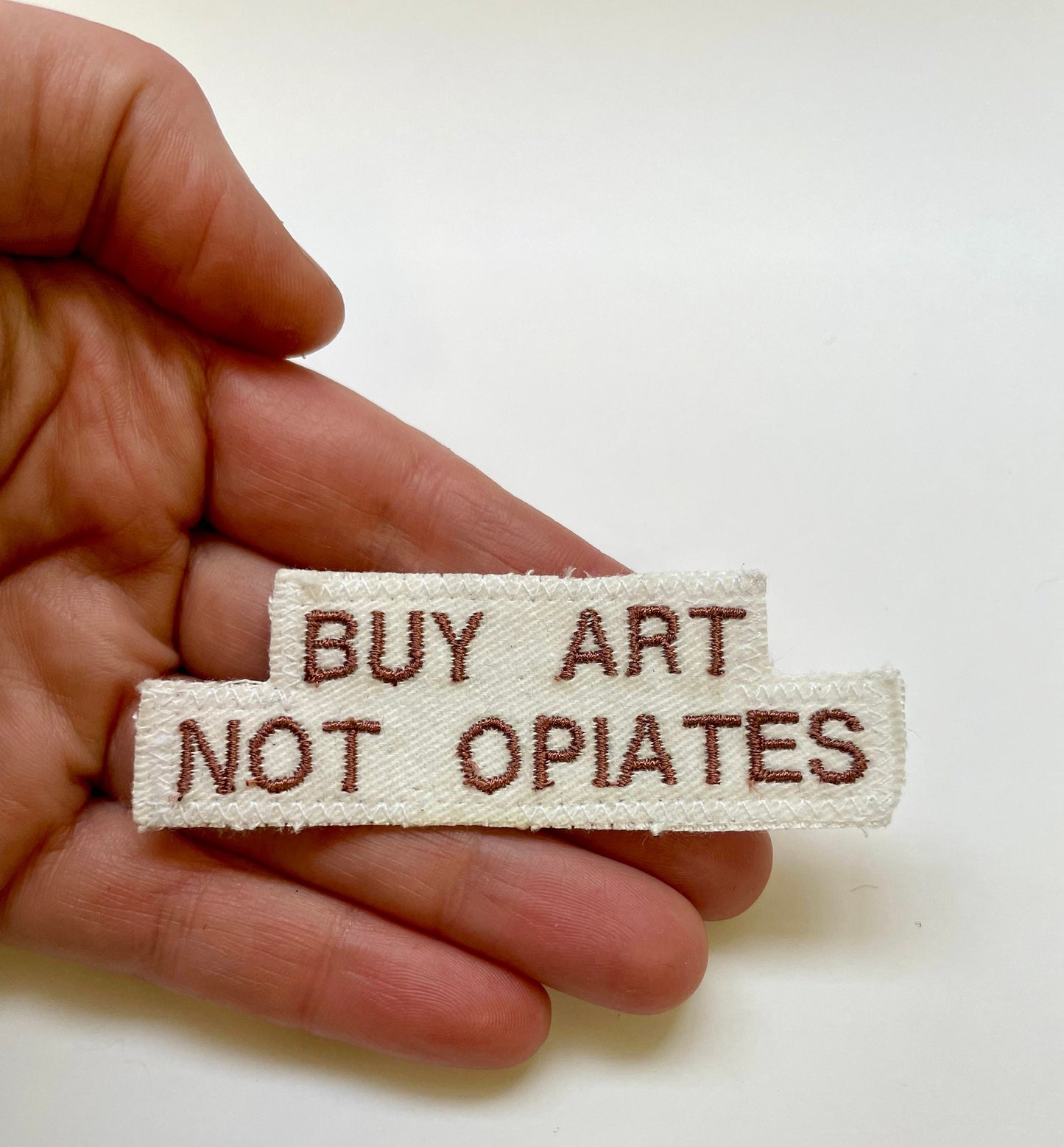 a hand holding a white piece of cloth that says buy art not opiates