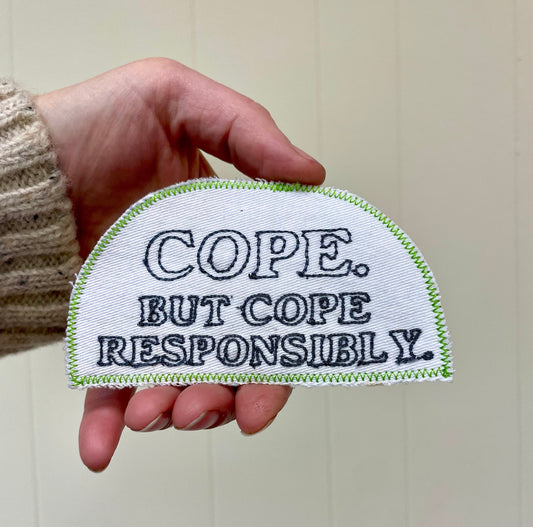 a hand holding a patch that says, cope but cope responsiblely