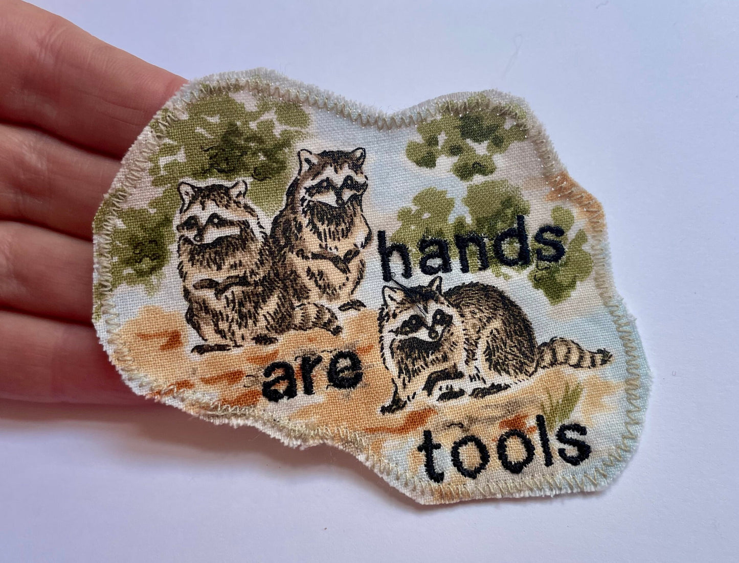 a hand holding a patch with a picture of raccoons on it